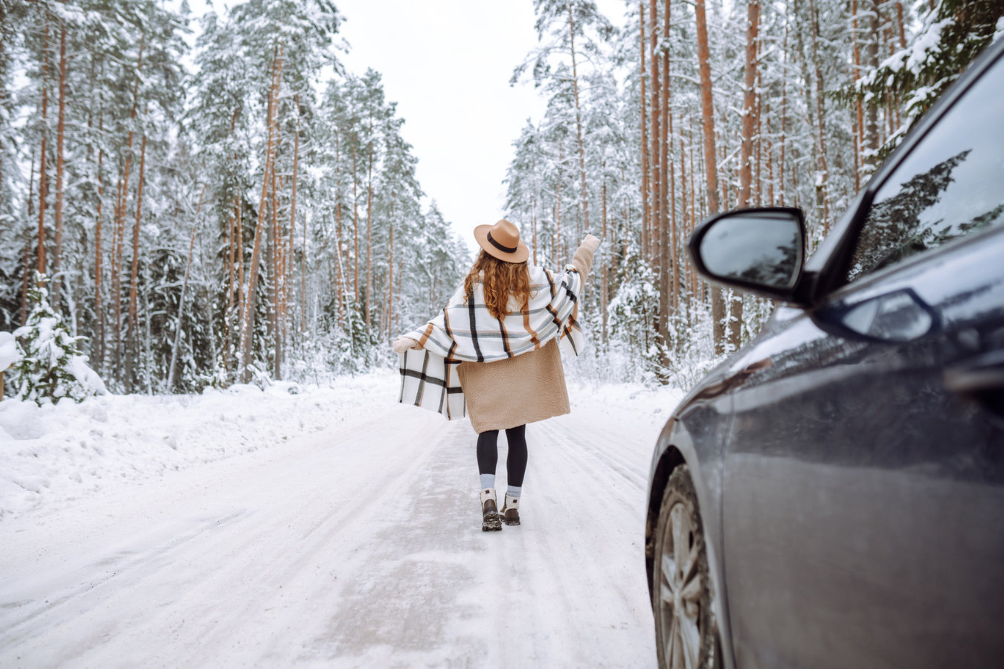 Женщина возле своего автомобиля в зимнее время наслаждается первым снегом на лесной дороге. Источник: Shutterstock