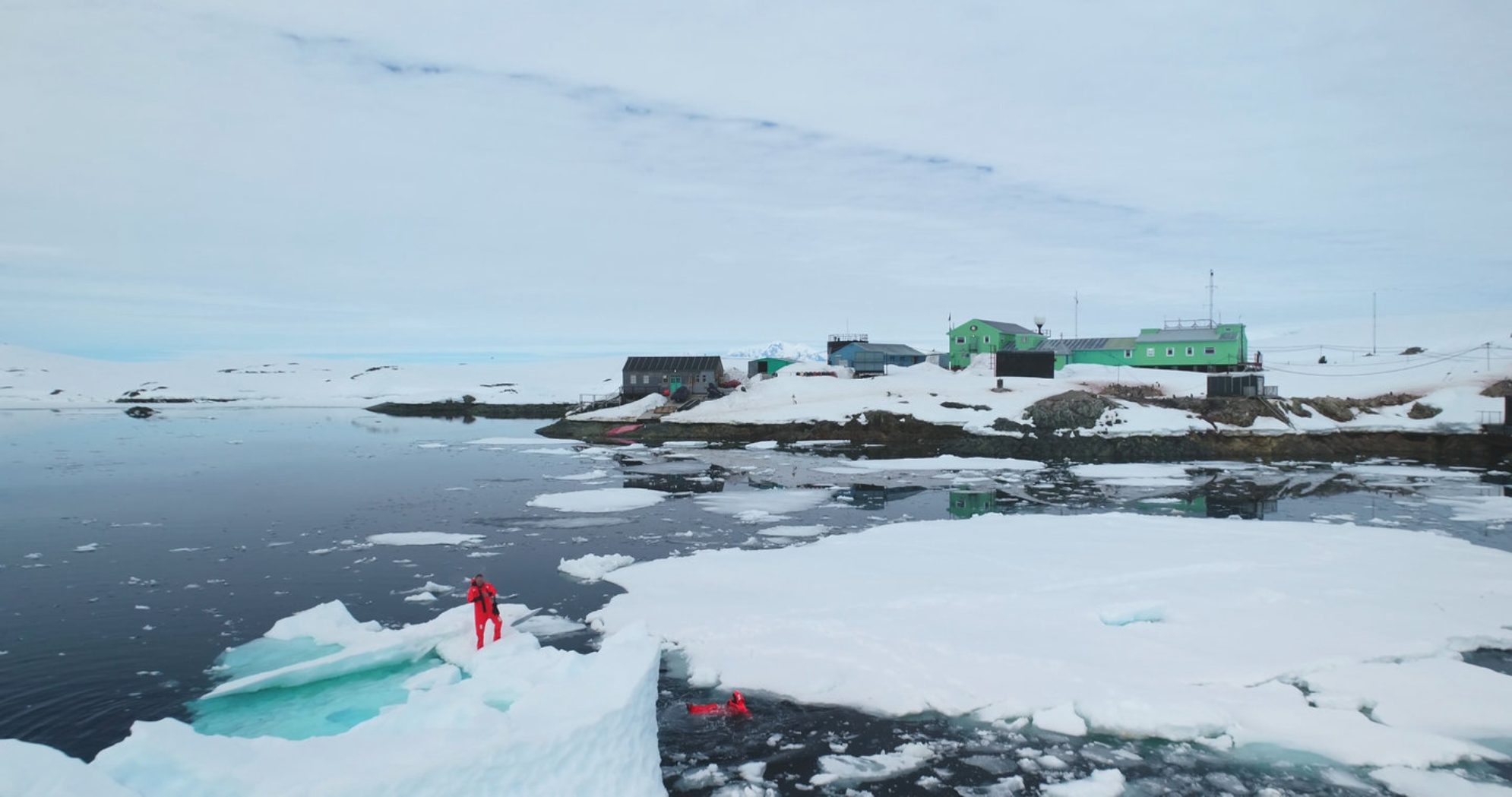 Ученые в оранжевых гидрокостюмах берут пробы океанской воды, стоя на тающей льдине. Экспедиция на полярную станцию. shutterstock.com