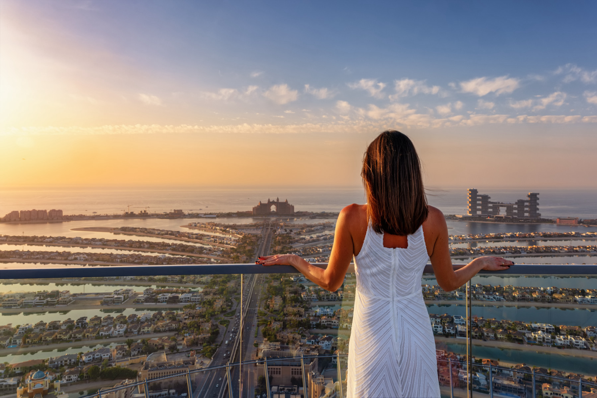 Девушка в белом платье наслаждается закатом над островом Пальма в Дубае, ОАЭ Shutterstock
