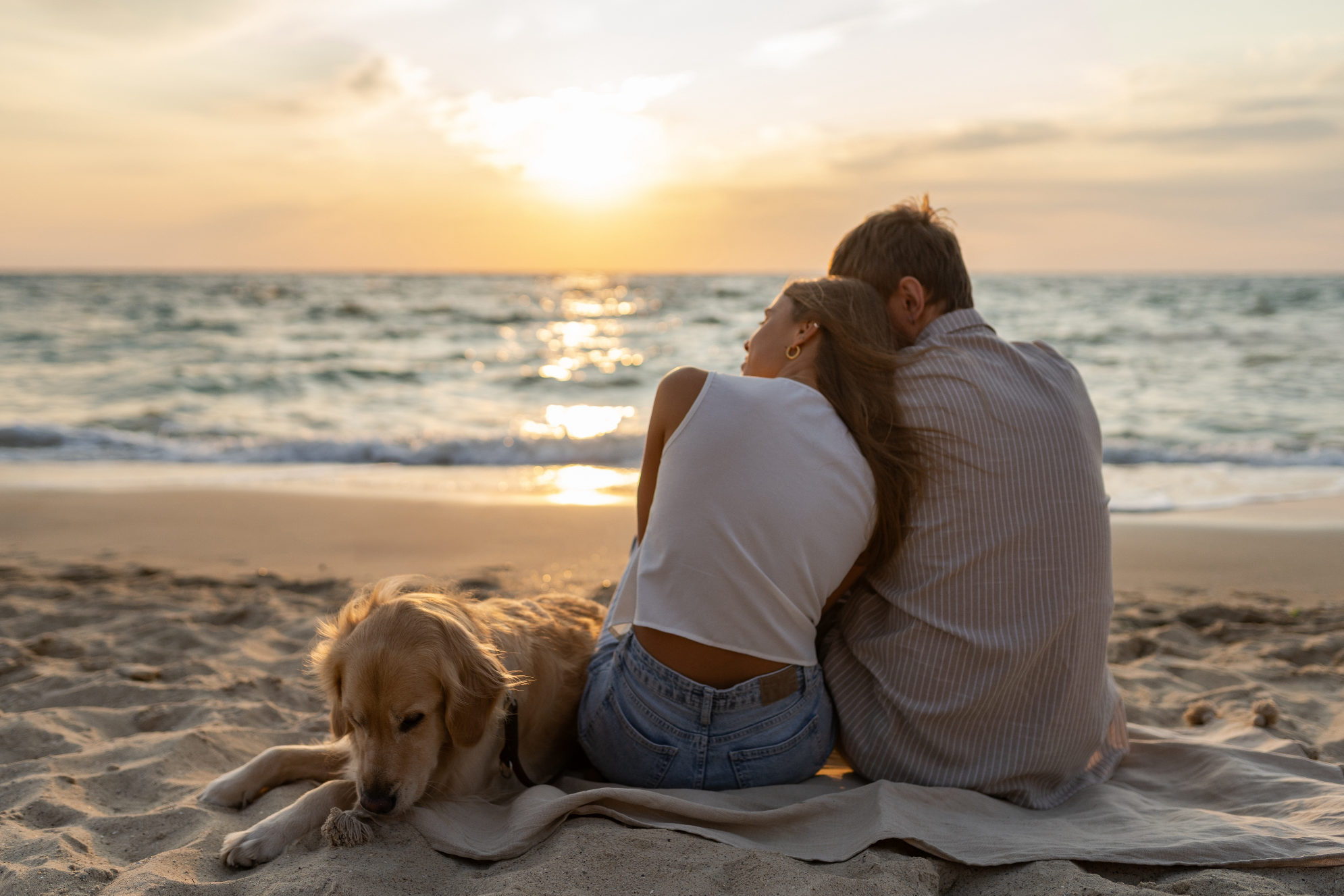 Семейная пара со своим четвероногим другом отдыхают на берегу моря. Источник: Shutterstock