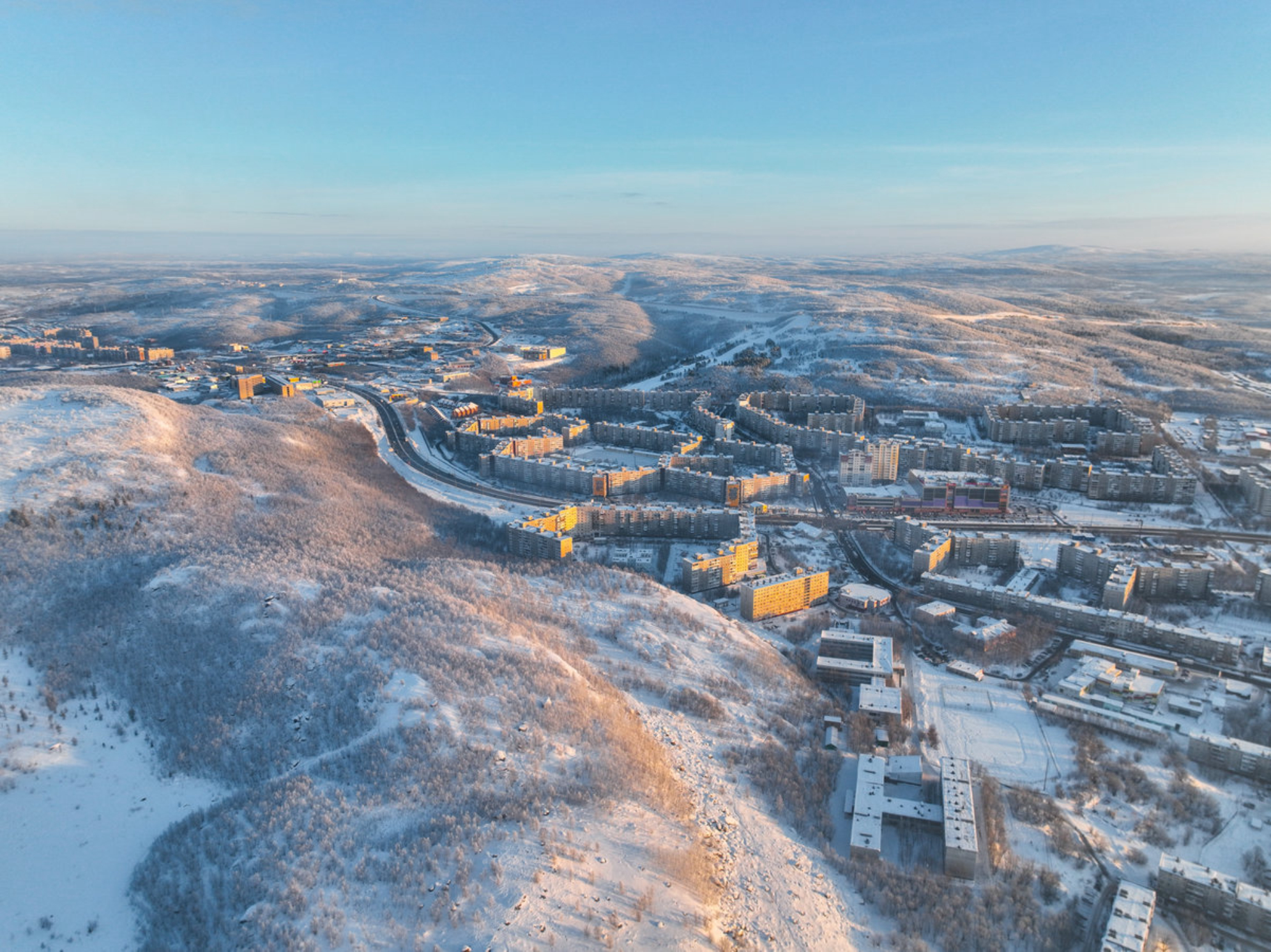 Вид с воздуха на жилой район Мурманска с заснеженными зданиями и деревьями под ясным зимним небом, Россия. Источник: Shutterstock