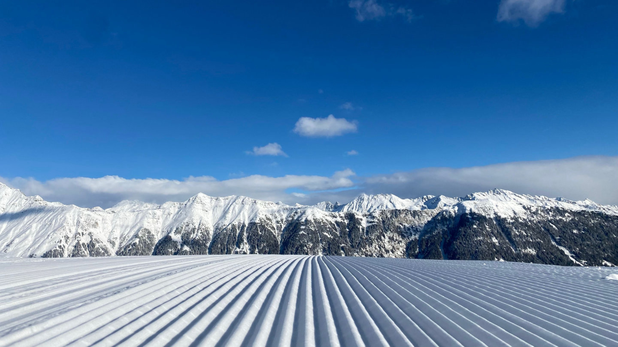 Снимок лыжного курорта Роза Хутор со слоями снега на фоне голубого неба и гор. Источник: Shutterstock