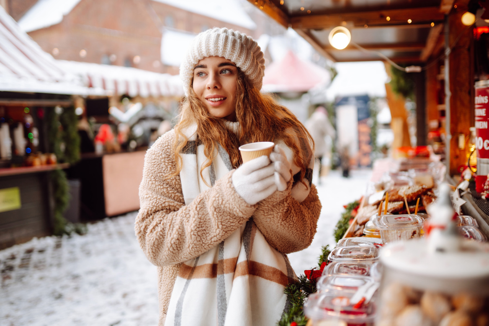 Девушка держит в руках стаканчик с согревающим напитком на зимней ярмарке. Источник: Shutterstock