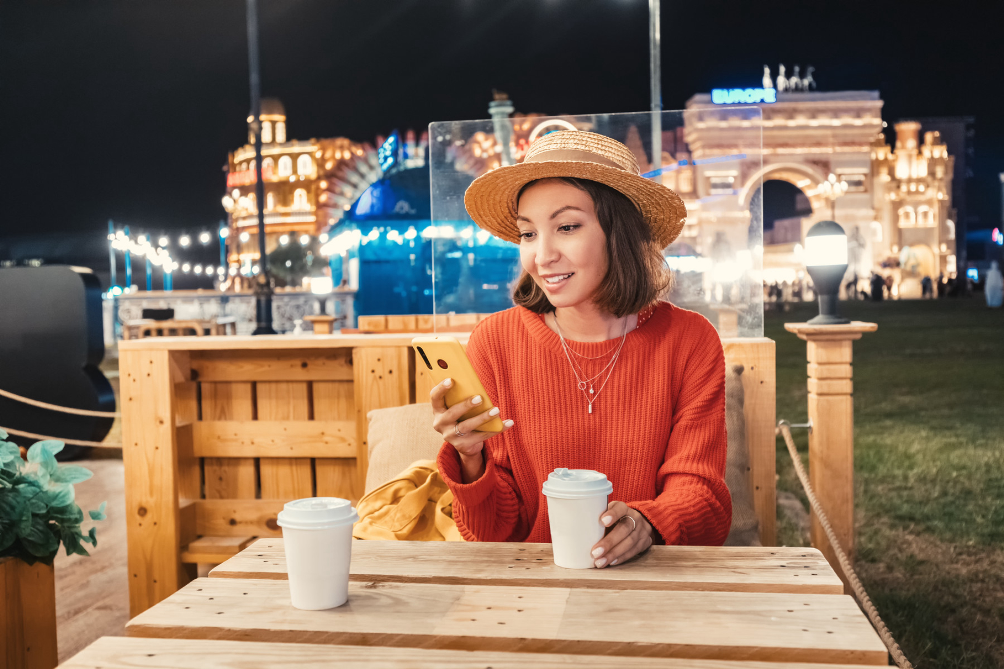 Девушка читает свои социальные сети на смартфоне и пьет кофе в уличном кафе в районе Global Village в Дубае Shutterstock