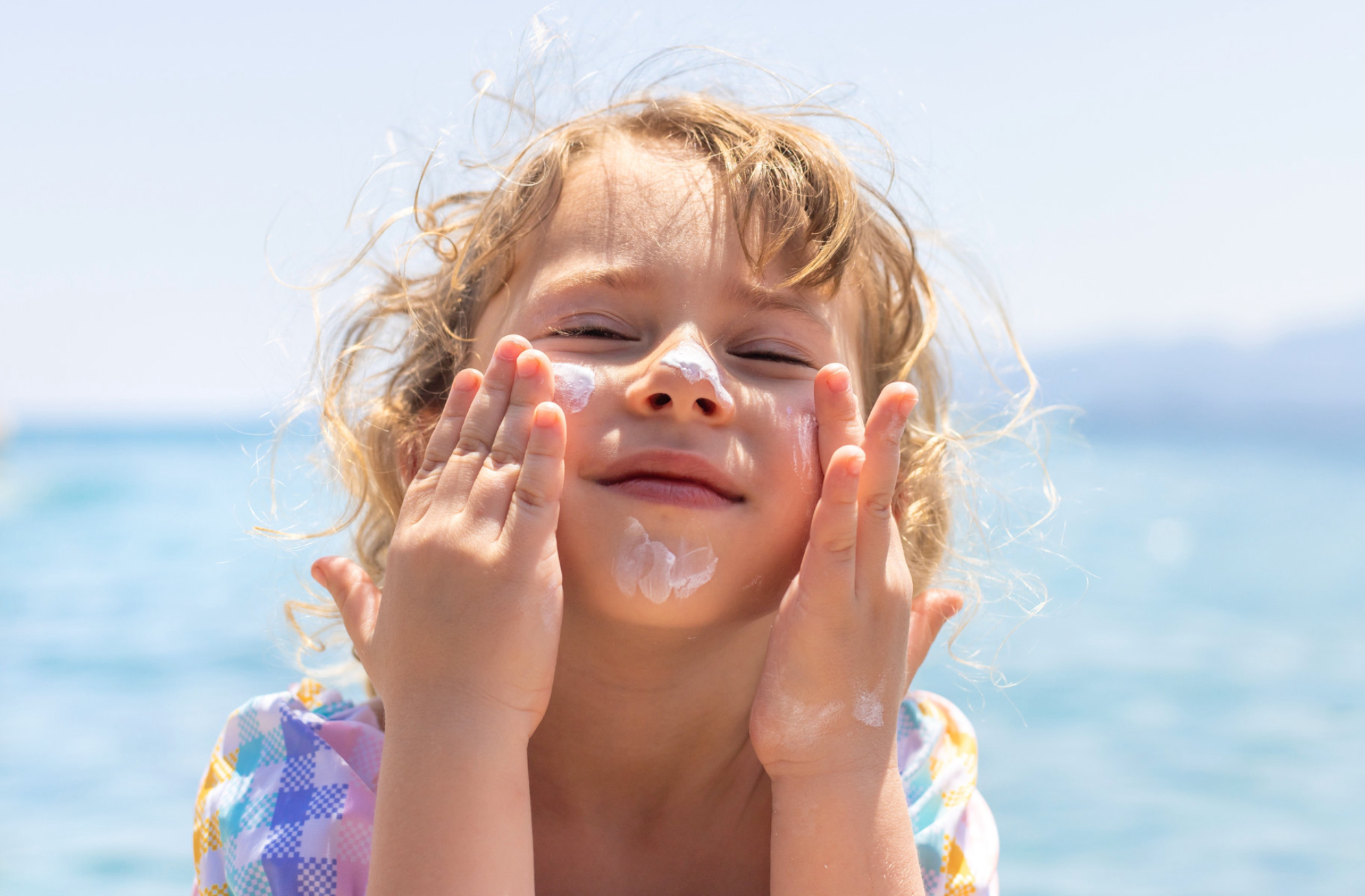 Ребенок мажет на лицо солнцезащитный крем. Источник: Shutterstock