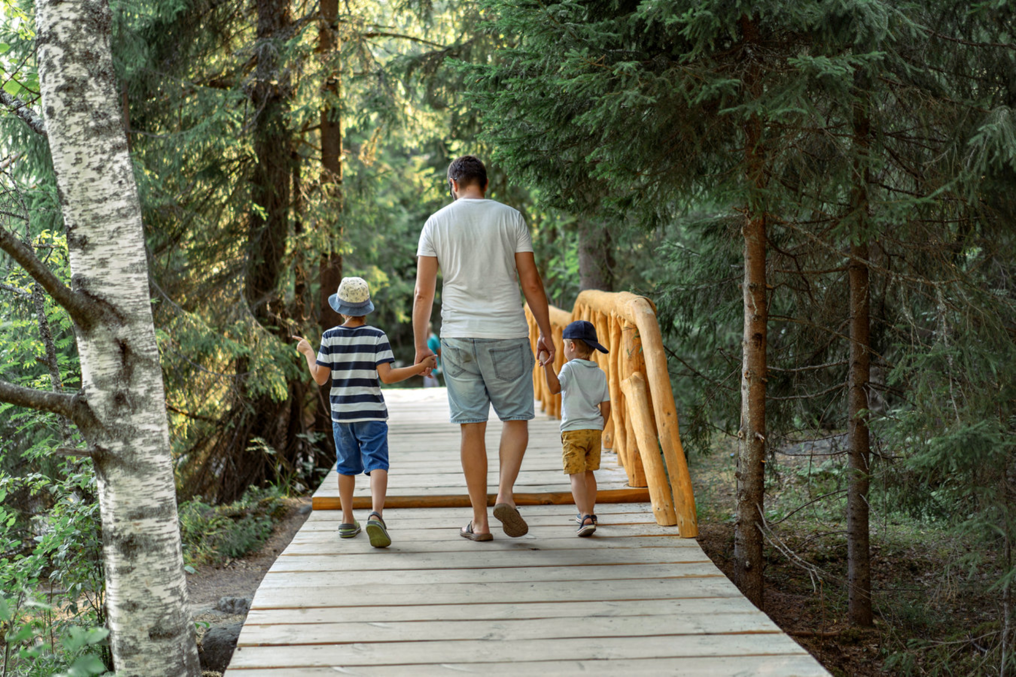 Отец с двумя детьми гуляет по деревянной дорожке в парке. Рускеальские водопады, Карелия, Россия Shutterstock